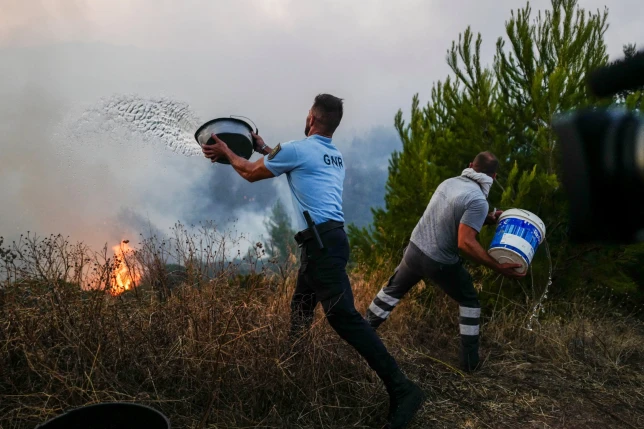 A police officer and a local resident throw buckets of water at the wildfire in Cascais, Portugal